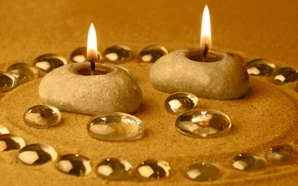 A serene HD desktop wallpaper featuring two candlelit stones surrounded by smooth glass pebbles on a sandy surface, creating a calming and elegant atmosphere.