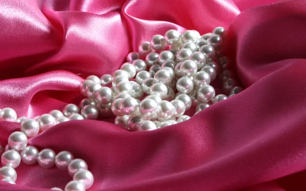 A close-up of elegant white pearls scattered over luxurious pink satin fabric, creating a striking visual for a high-definition desktop wallpaper or background.