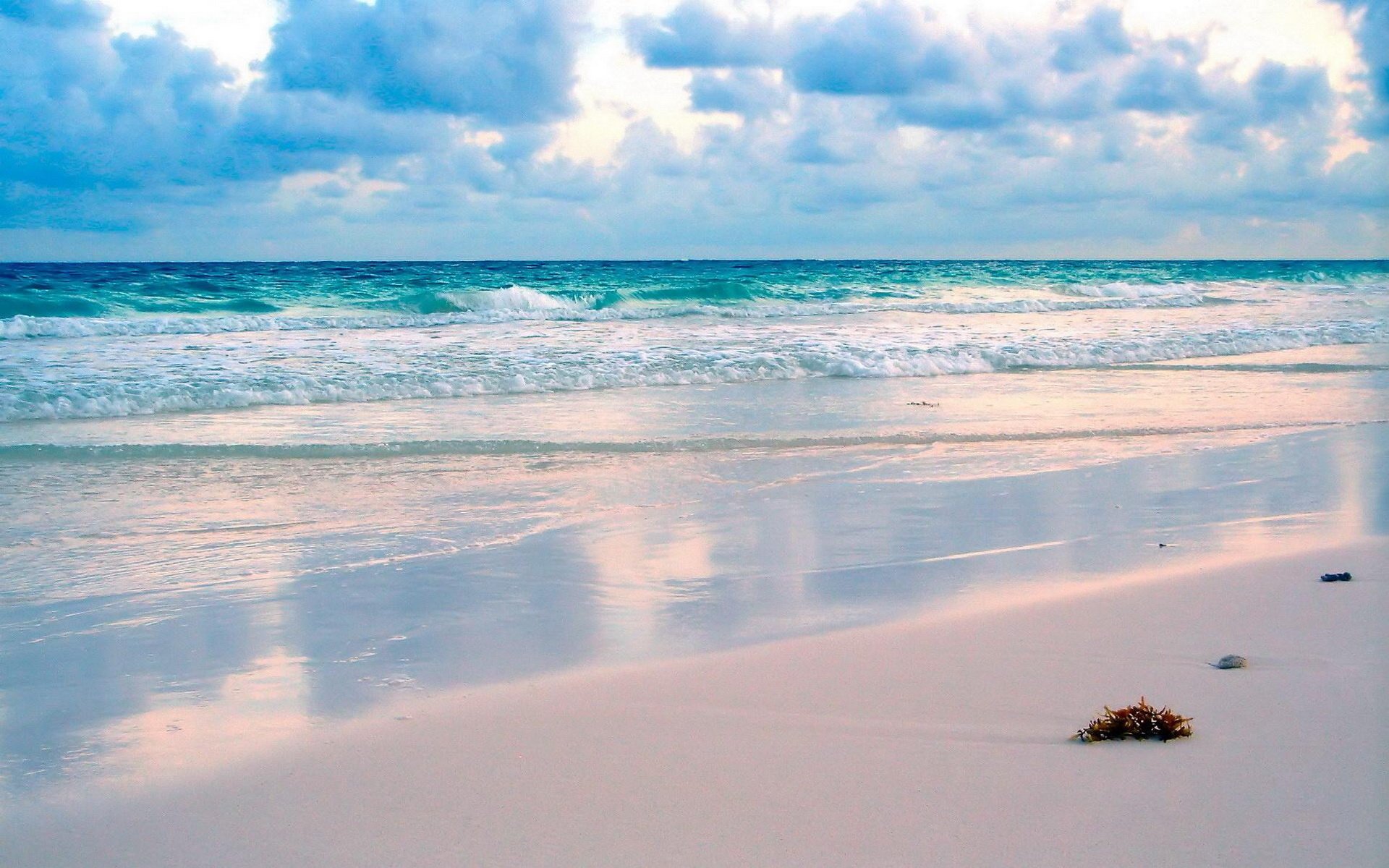 HD PC desktop wallpaper of a serene beach with gentle waves, soft sand, and a partly cloudy sky reflecting on the wet shore.