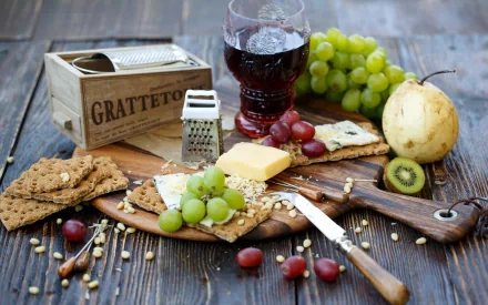 A still life composition featuring a wooden board with crackers, cheese, grapes, and a pear, accompanied by a glass of red wine, set against a rustic background.