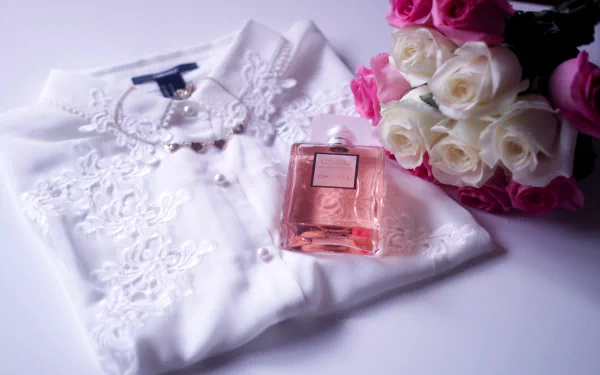 A flat lay featuring an elegant white blouse, a delicate necklace, a bottle of perfume, and a bouquet of roses, showcasing a blend of photography and style in a serene HD desktop wallpaper.