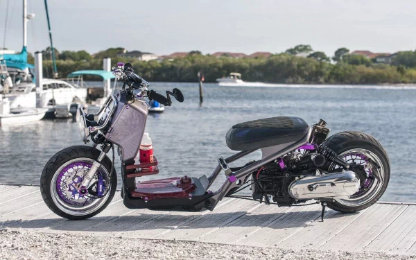 Custom Honda Ruckus scooter parked on a sunlit dock by a marina with boats and shoreline, HD PC desktop wallpaper and background.