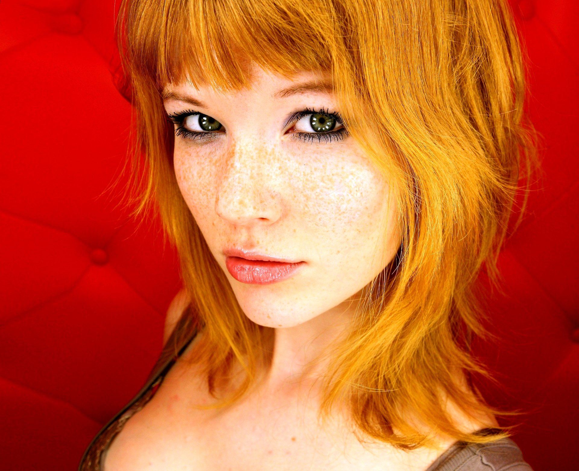HD PC desktop wallpaper featuring a close-up portrait of a woman with red hair and green eyes against a vibrant red background.