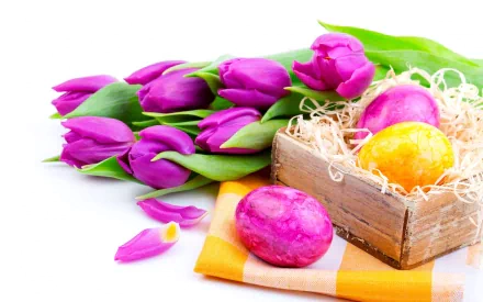 Colorful Easter eggs in a wooden box, surrounded by vibrant purple tulips and petals, create a festive holiday atmosphere. This HD wallpaper adds a cheerful touch to any desktop background.