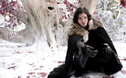 A high-definition desktop wallpaper featuring Kit Harington as Jon Snow from the TV show Game of Thrones, sitting in a snowy, forested setting with a large tree in the background.