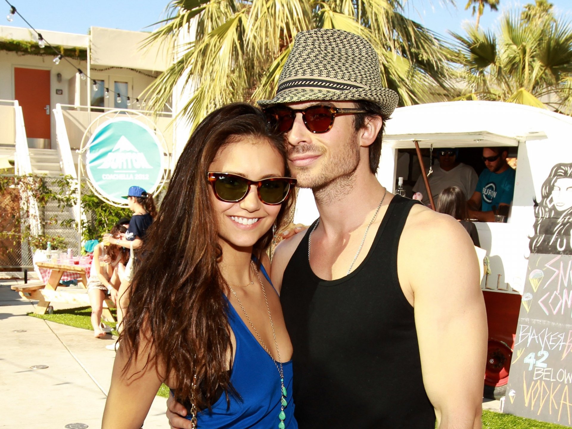 HD PC desktop wallpaper featuring celebrity actor Nina Dobrev and a male companion outdoors with palm trees and sunny weather in the background.