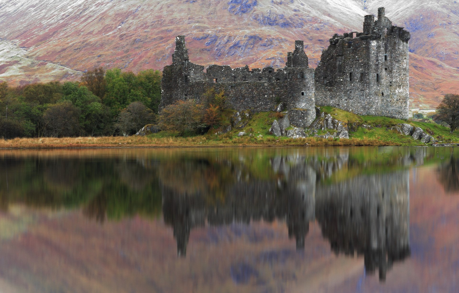 HD desktop wallpaper of an ancient man-made ruin reflecting in calm lake waters, set against a backdrop of lush greenery and a mountain landscape.