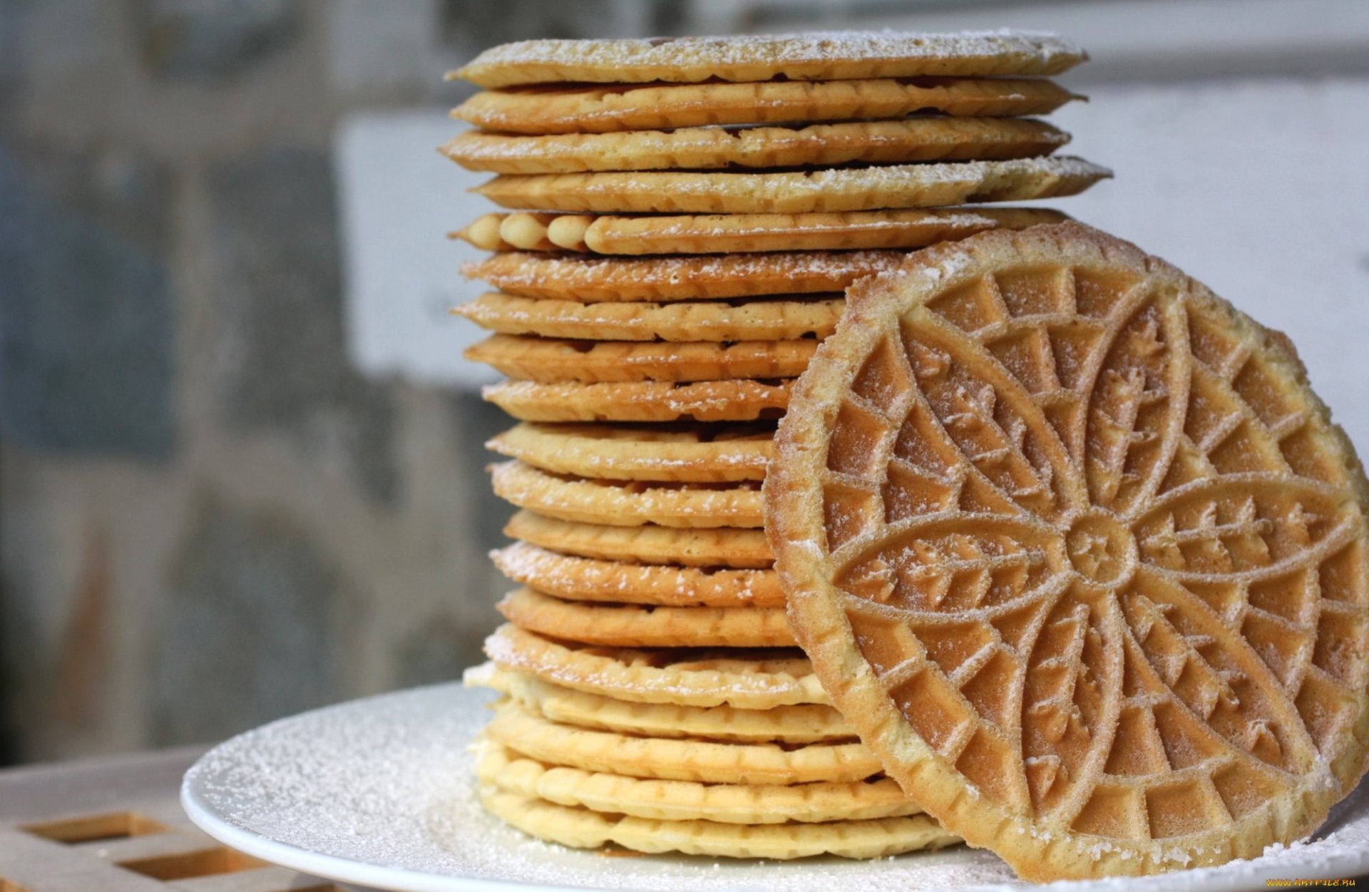 A stack of golden, intricately patterned cookies dusted with powdered sugar, set on a plate with a blurred background, creating a delightful food-themed desktop wallpaper.