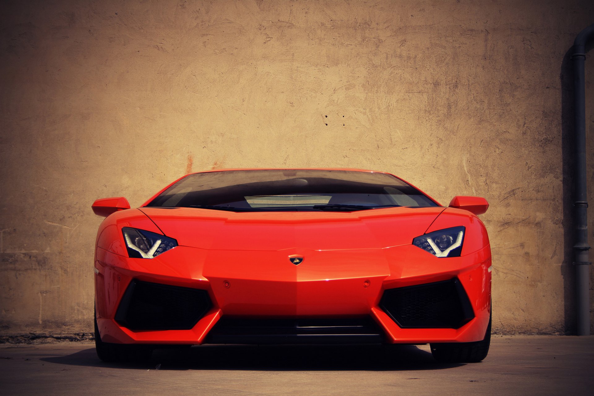 HD PC desktop wallpaper featuring a vibrant red Lamborghini Aventador parked against a textured beige wall, showcasing the vehicle's sleek front design.