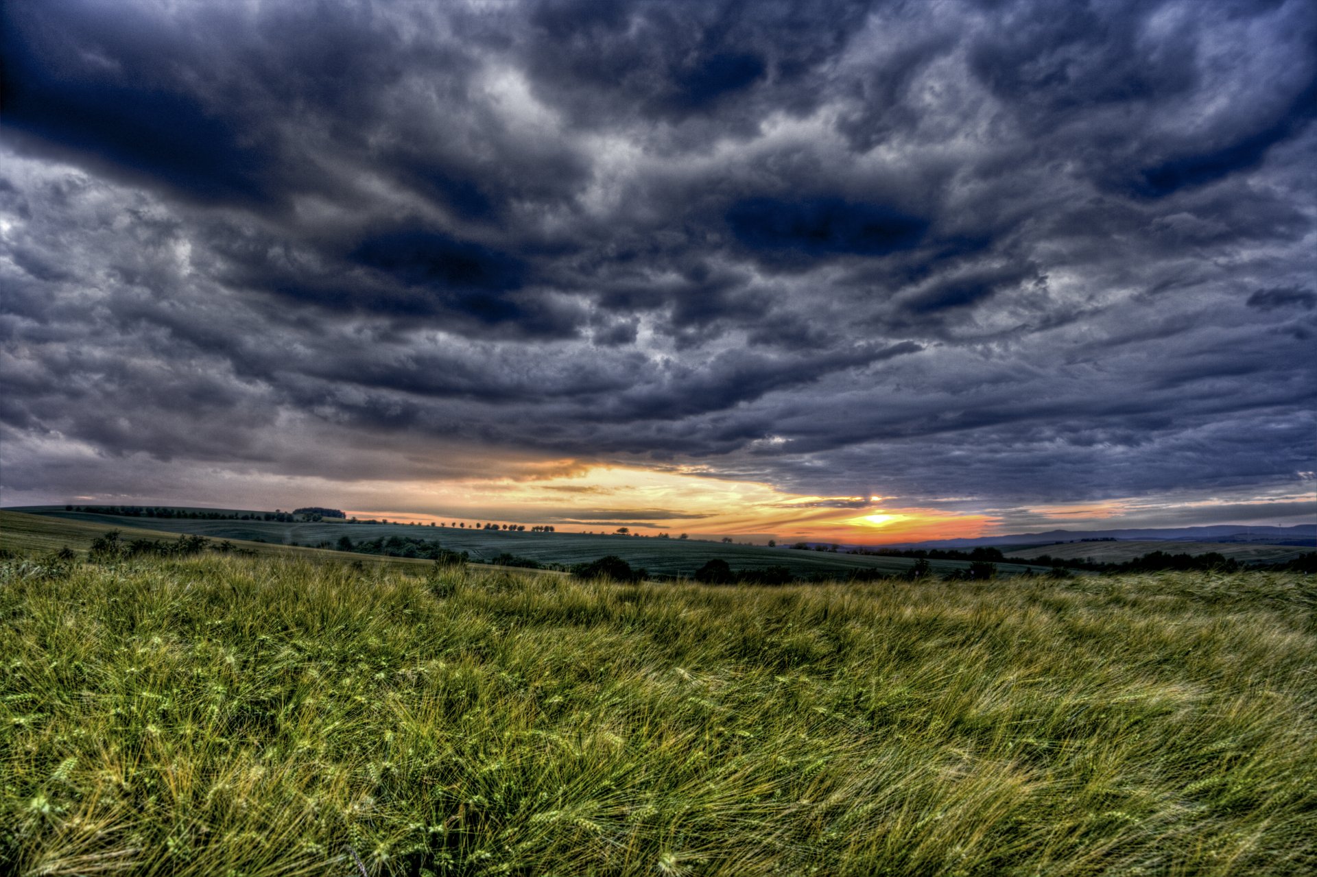 4K Ultra HD desktop wallpaper capturing a vast, grassy field under a dramatic cloudy sky at sunset, showcasing the beauty of nature.