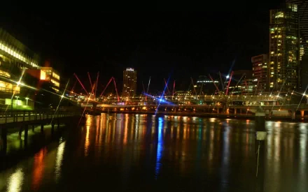Night view of Brisbane's Kurilpa Bridge and city buildings reflecting vibrant lights on the water, captured in HD for a striking desktop wallpaper background.