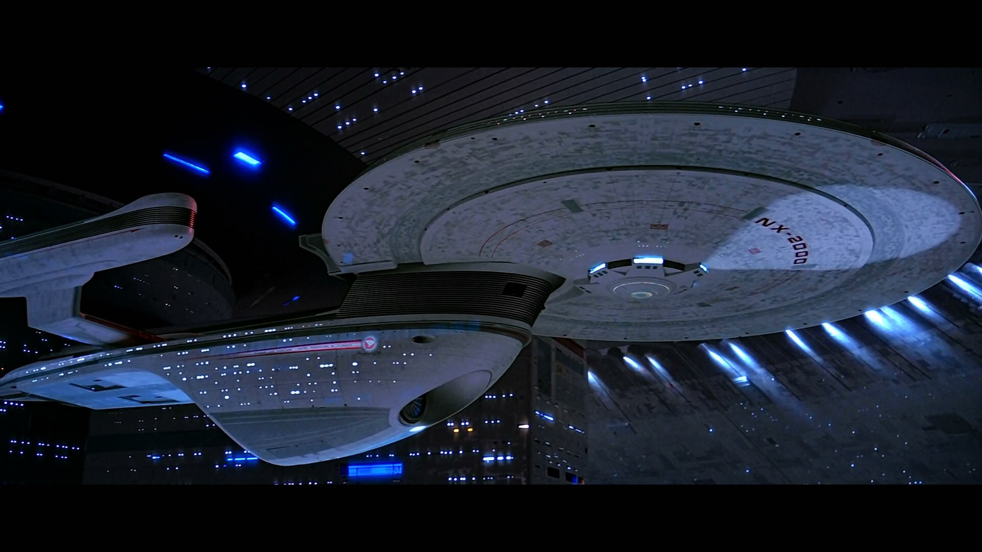 A stunning HD desktop wallpaper featuring a Star Trek-inspired spaceship, illuminated by stars and sleek blue lights, set against a backdrop of deep space.
