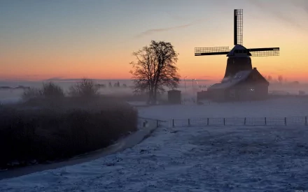 HD desktop wallpaper showcasing a man-made windmill standing amid a misty landscape at sunrise, blending natural beauty with historic architecture.