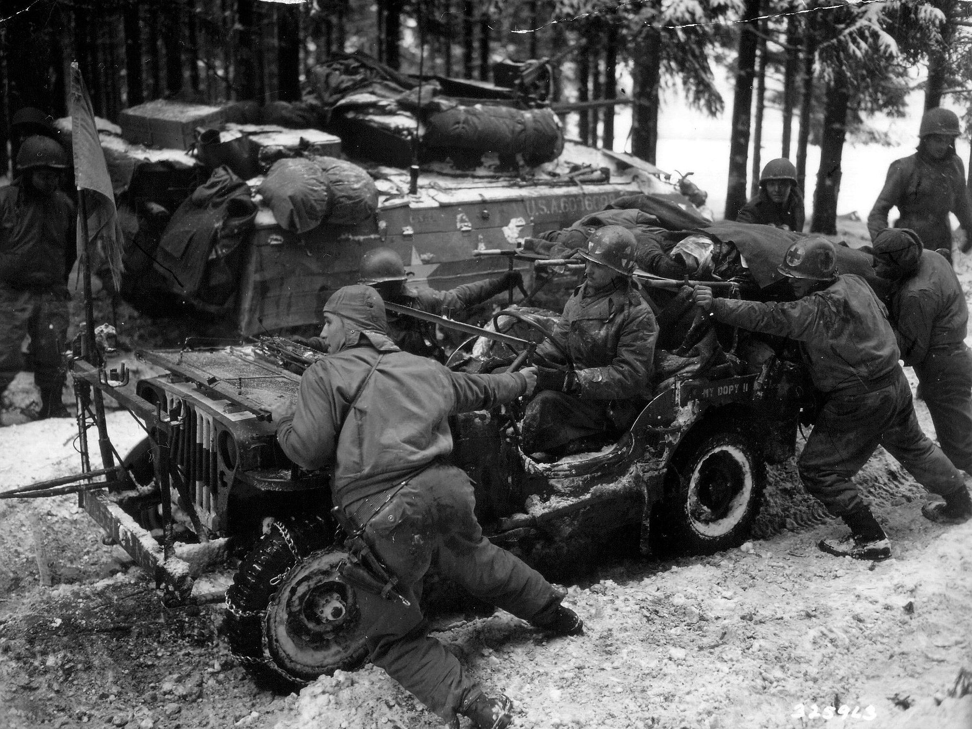 Soldiers in winter gear work on a damaged jeep, with a tank in the background, capturing a poignant moment from World War II in this HD desktop wallpaper.