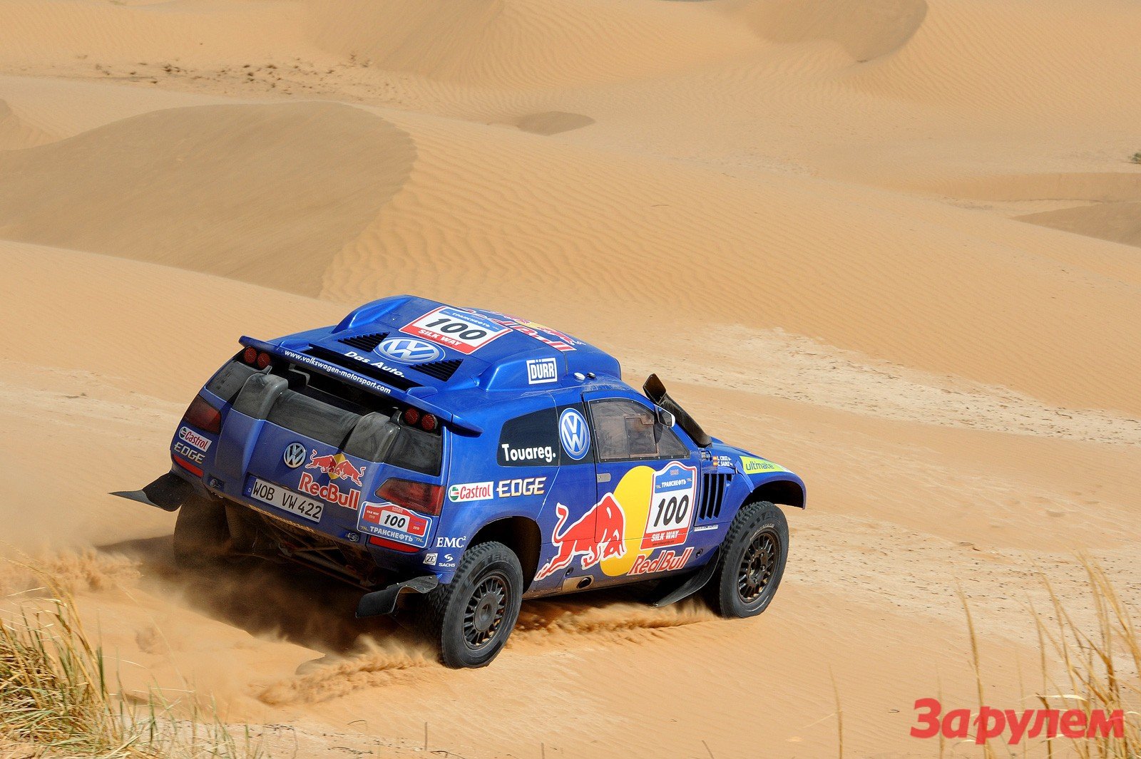HD PC desktop wallpaper/background: blue Volkswagen Touareg rally vehicle with Red Bull livery kicking up sand as it races across golden desert dunes.