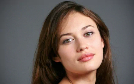 HD desktop wallpaper featuring Olga Kurylenko, showcasing her captivating gaze and natural beauty against a simple gray background.