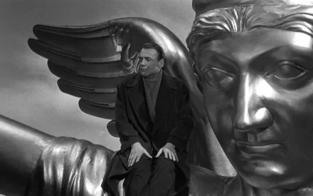 HD desktop wallpaper featuring a black-and-white scene from Wings of Desire with a man seated next to a large sculpted angel wing.