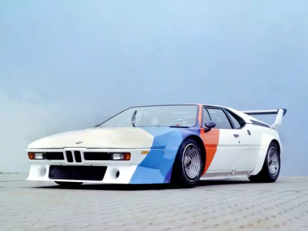 HD PC desktop wallpaper of a white BMW M1 sports car with blue and red accent panels, low stance and prominent rear wing against a pale sky.
