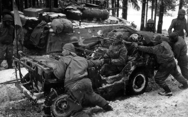 Soldiers in winter gear work on a damaged jeep, with a tank in the background, capturing a poignant moment from World War II in this HD desktop wallpaper.