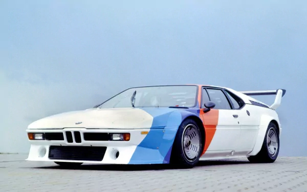 HD PC desktop wallpaper of a white BMW M1 sports car with blue and red accent panels, low stance and prominent rear wing against a pale sky.