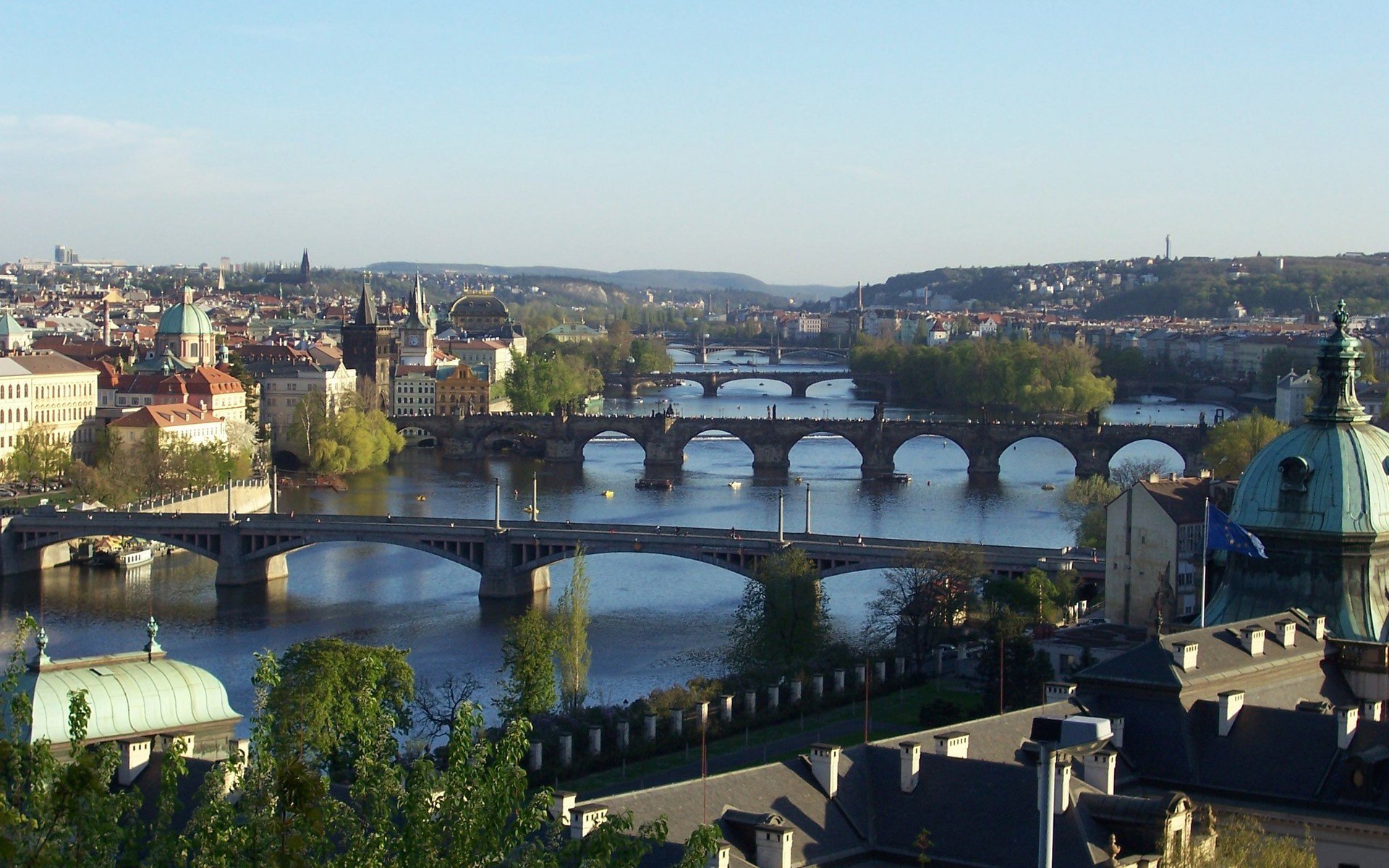 HD desktop wallpaper showcasing multiple man-made bridges spanning the Vltava River in Prague, Czech Republic, with the cityscape under a clear sky.