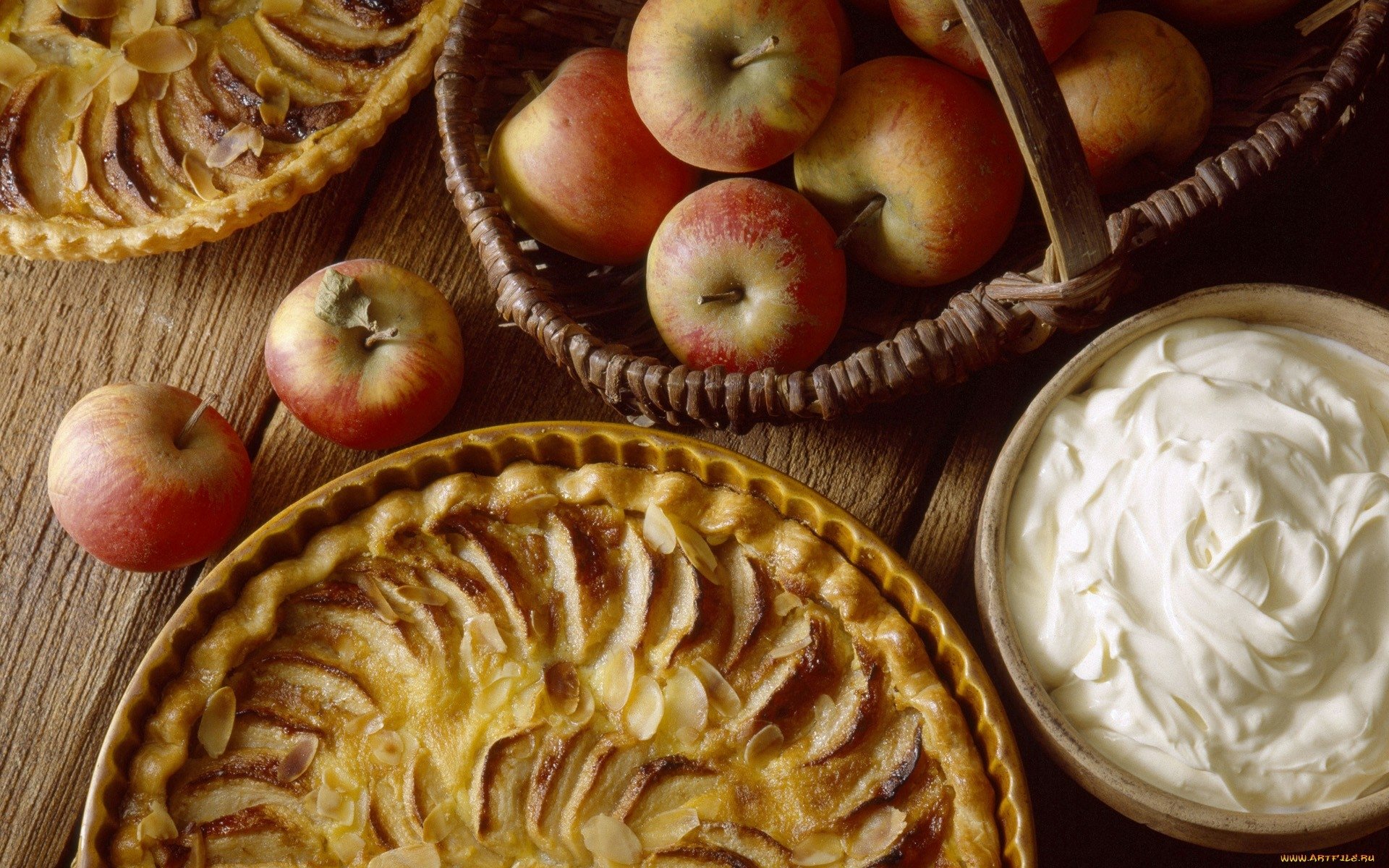 HD PC desktop wallpaper featuring a still life of freshly baked apple pies, a basket of apples, and a bowl of whipped cream on a wooden surface.