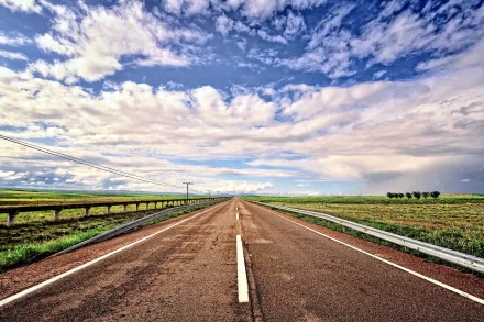 A scenic view of a straight road stretching into the horizon, surrounded by green fields under a dramatic sky, suitable as a high-definition desktop wallpaper or background.