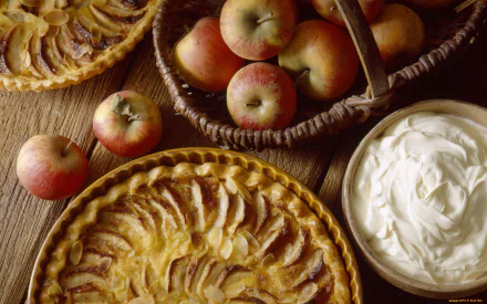 HD PC desktop wallpaper featuring a still life of freshly baked apple pies, a basket of apples, and a bowl of whipped cream on a wooden surface.