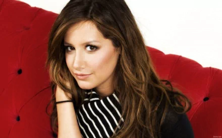 HD desktop wallpaper featuring celebrity Ashley Tisdale posing on a red cushioned background with a striped black and white top.