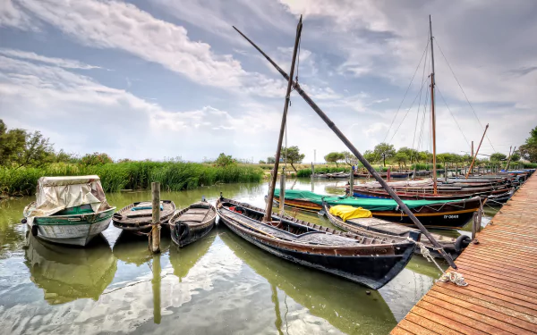 HD desktop wallpaper of various boats docked along a wooden pier on calm water under a partly cloudy sky.
