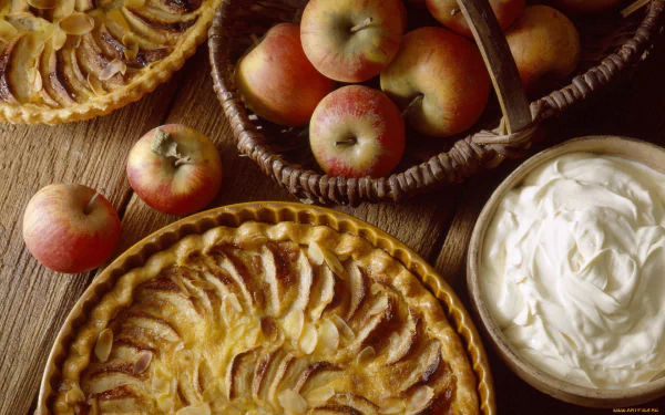 HD PC desktop wallpaper featuring a still life of freshly baked apple pies, a basket of apples, and a bowl of whipped cream on a wooden surface.