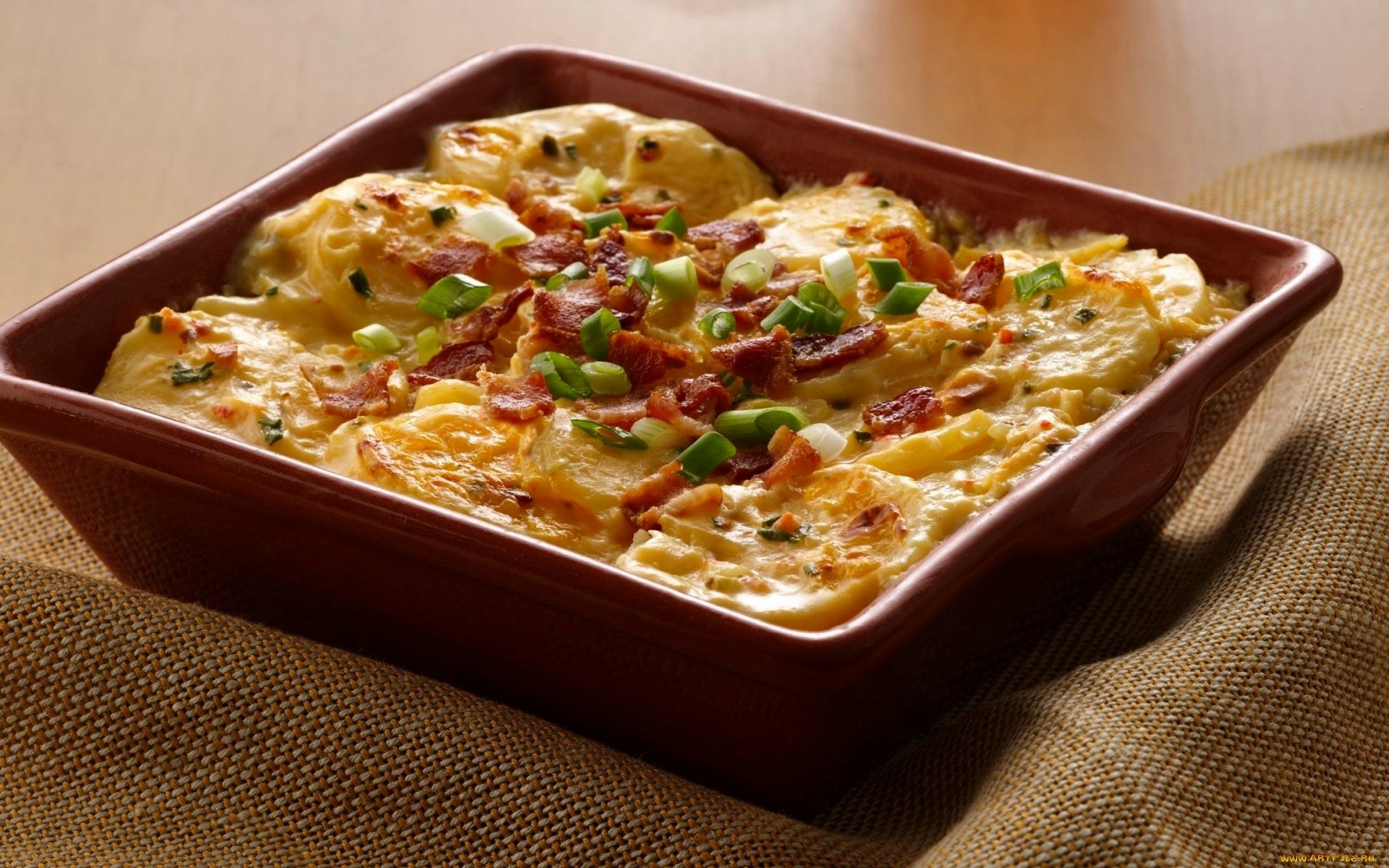 HD PC desktop wallpaper showing a baked cheesy potato casserole topped with chopped green onions and crispy bacon bits.