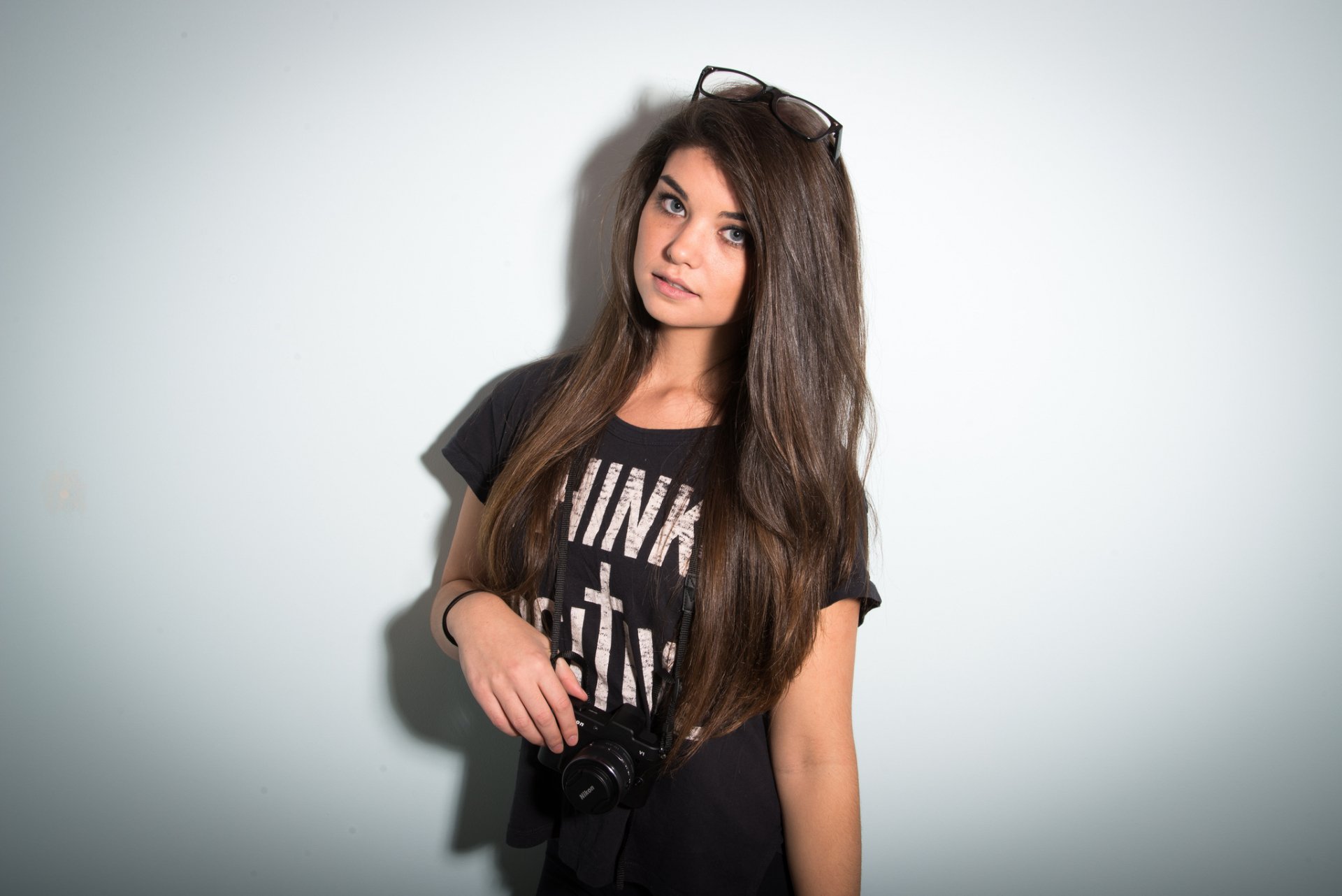 HD desktop wallpaper featuring a woman model with long dark hair, wearing a black t-shirt and holding a camera.