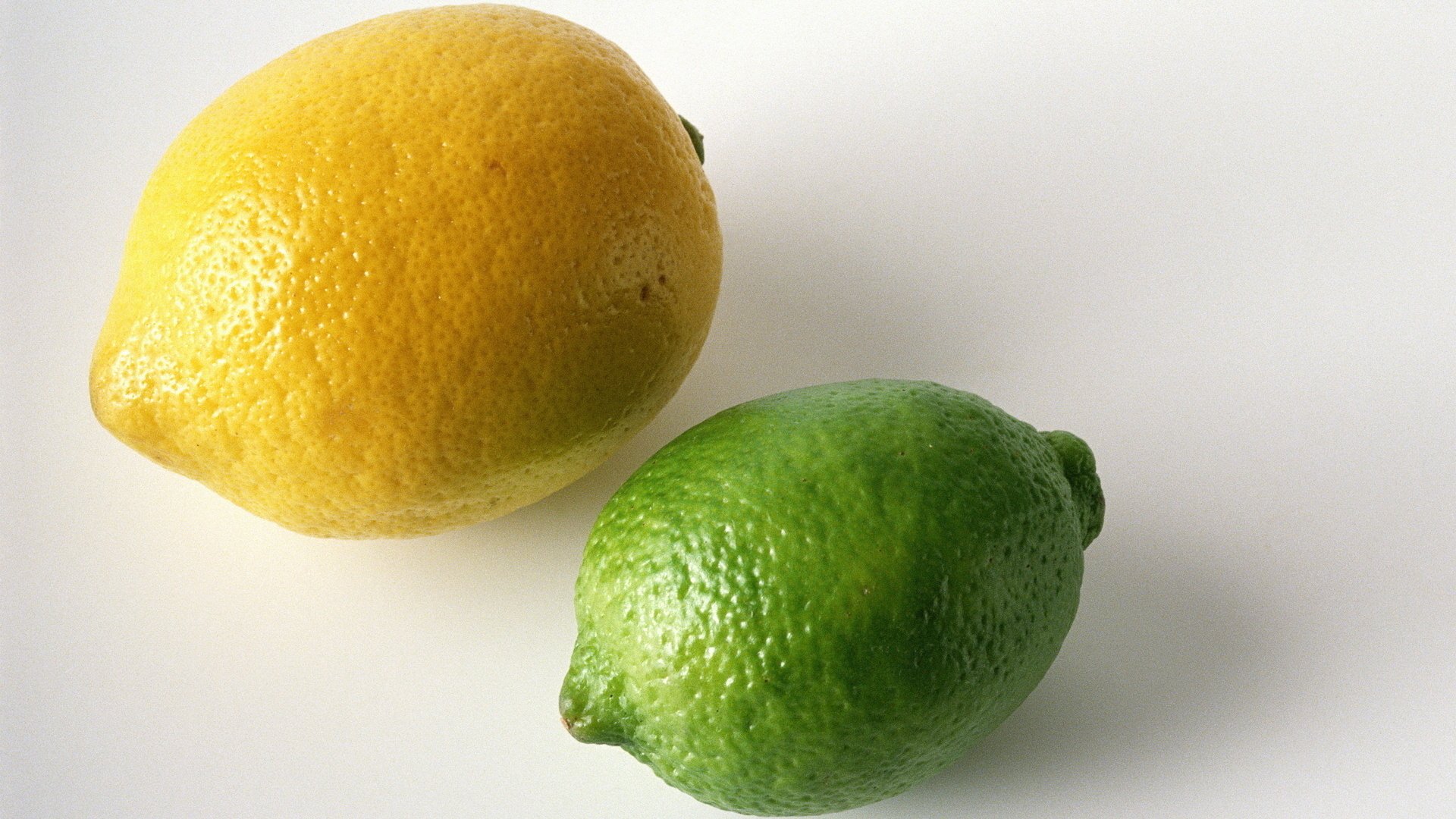 HD PC desktop wallpaper featuring a close-up of a yellow lemon and a green lime on a clean white background.