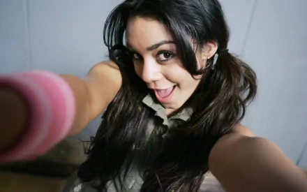 A cheerful Vanessa Hudgens takes a playful selfie, showcasing her long dark hair and a fun, casual style. This vibrant image serves as an engaging desktop wallpaper.