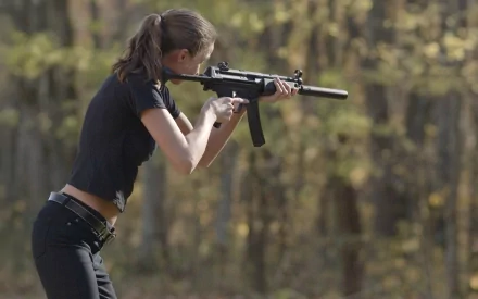 A woman aims a firearm in a natural outdoor setting, showcasing strength and focus. This HD desktop wallpaper captures the theme of Girls & Guns.