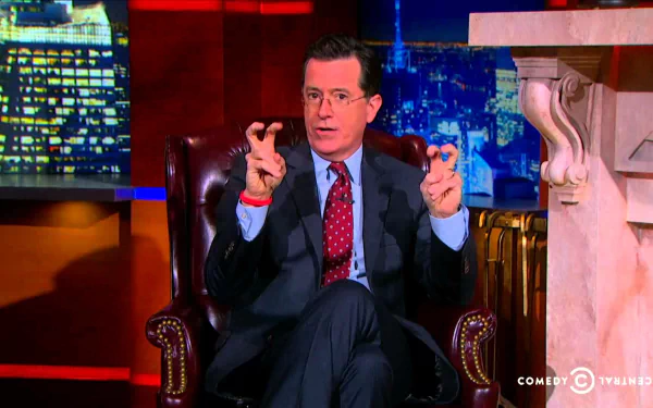 HD wallpaper of a man from The Colbert Report seated, making air quotes, with the show's set in the background.