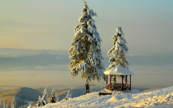 A tranquil winter landscape features snow-covered trees and a gazebo, with serene mountains in the background, creating a beautiful HD desktop wallpaper.
