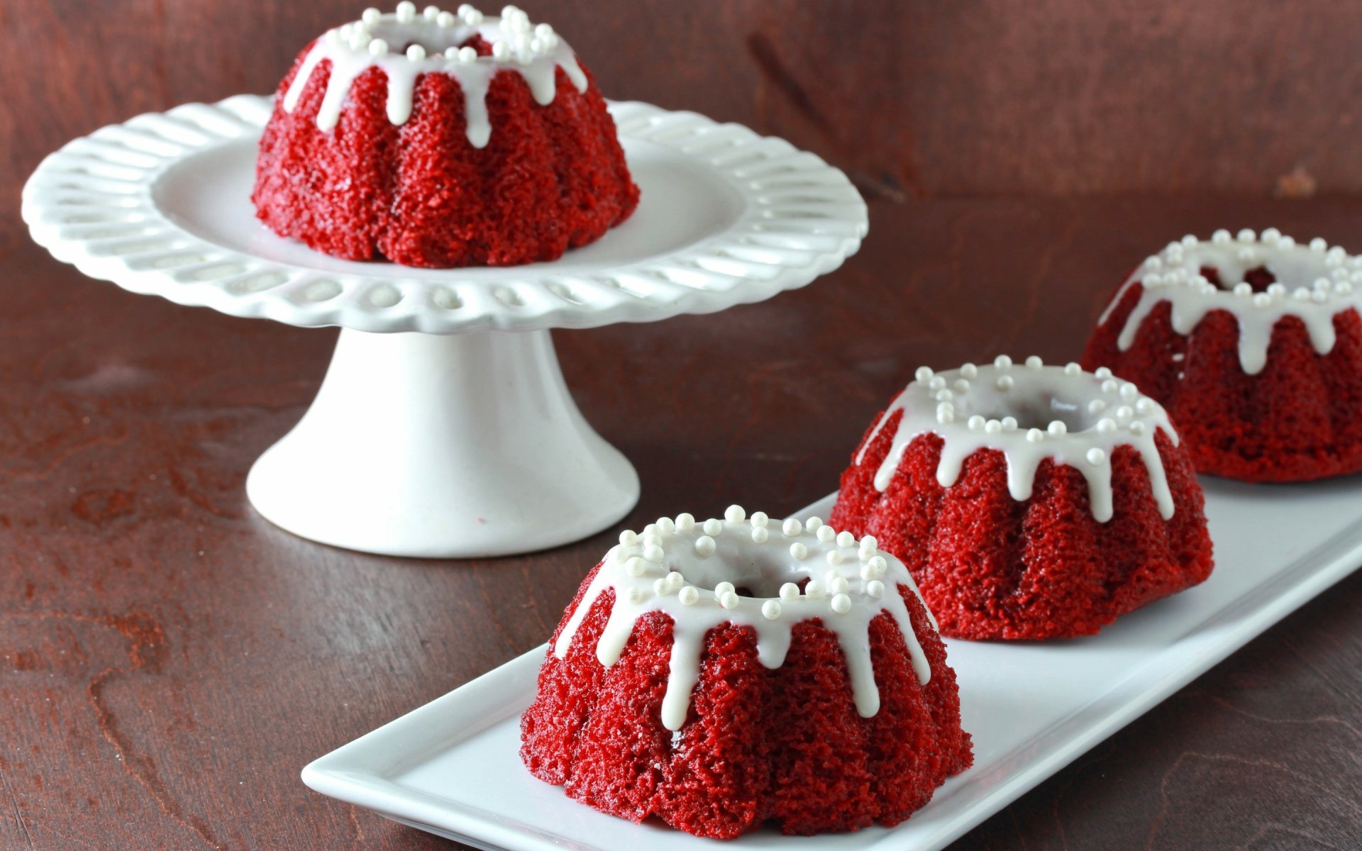 A colorful display of red velvet mini cakes topped with white icing and decorative sprinkles, serving as a delightful dessert background for any sweet-themed desktop wallpaper.