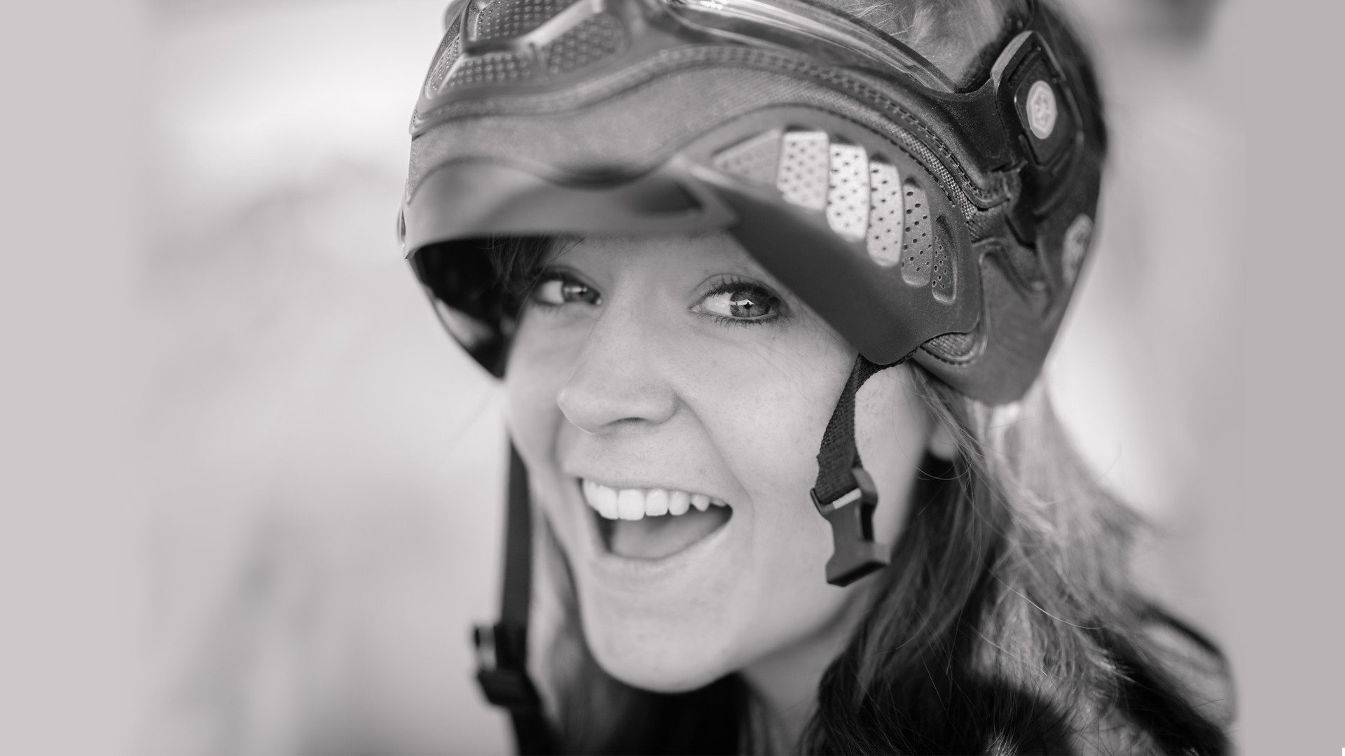 A cheerful woman wearing a helmet smiles brightly, embodying the spirit of music and adventure, set against a stylish HD PC desktop wallpaper background.