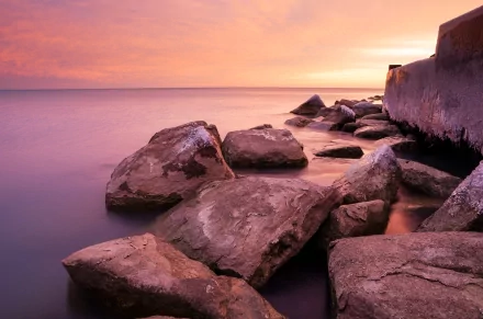 HD PC desktop wallpaper featuring large rocks along a serene shoreline at sunset, showcasing nature's calm and vibrant colors.