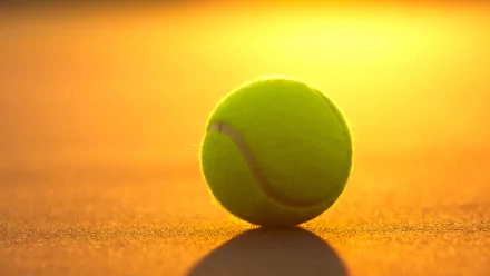 A vibrant yellow tennis ball sits on a court, illuminated by a warm sunset. This high-definition image captures the essence of the sport, making it a striking desktop wallpaper.