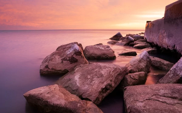 HD PC desktop wallpaper featuring large rocks along a serene shoreline at sunset, showcasing nature's calm and vibrant colors.