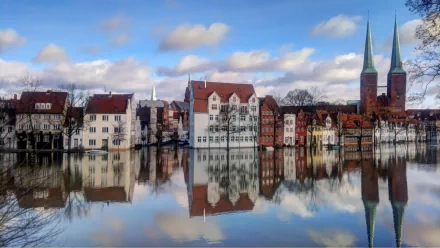 HD PC desktop wallpaper showcasing a serene man-made town with historic buildings and church spires reflected in calm waters under a partly cloudy sky.