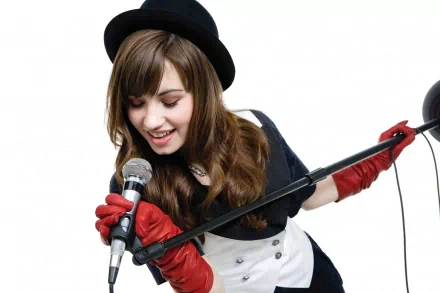 Demi Lovato performs passionately, wearing a black hat and red gloves, holding a microphone. This HD desktop wallpaper captures the vibrant energy of her music.
