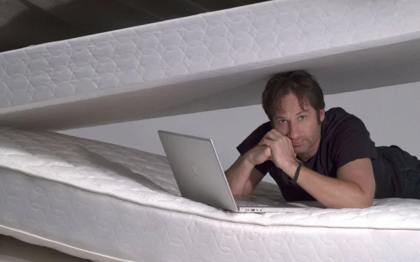 HD desktop wallpaper featuring celebrity David Duchovny lying between two mattresses with a laptop, showcasing a casual and contemplative pose.