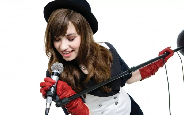 Demi Lovato performs passionately, wearing a black hat and red gloves, holding a microphone. This HD desktop wallpaper captures the vibrant energy of her music.