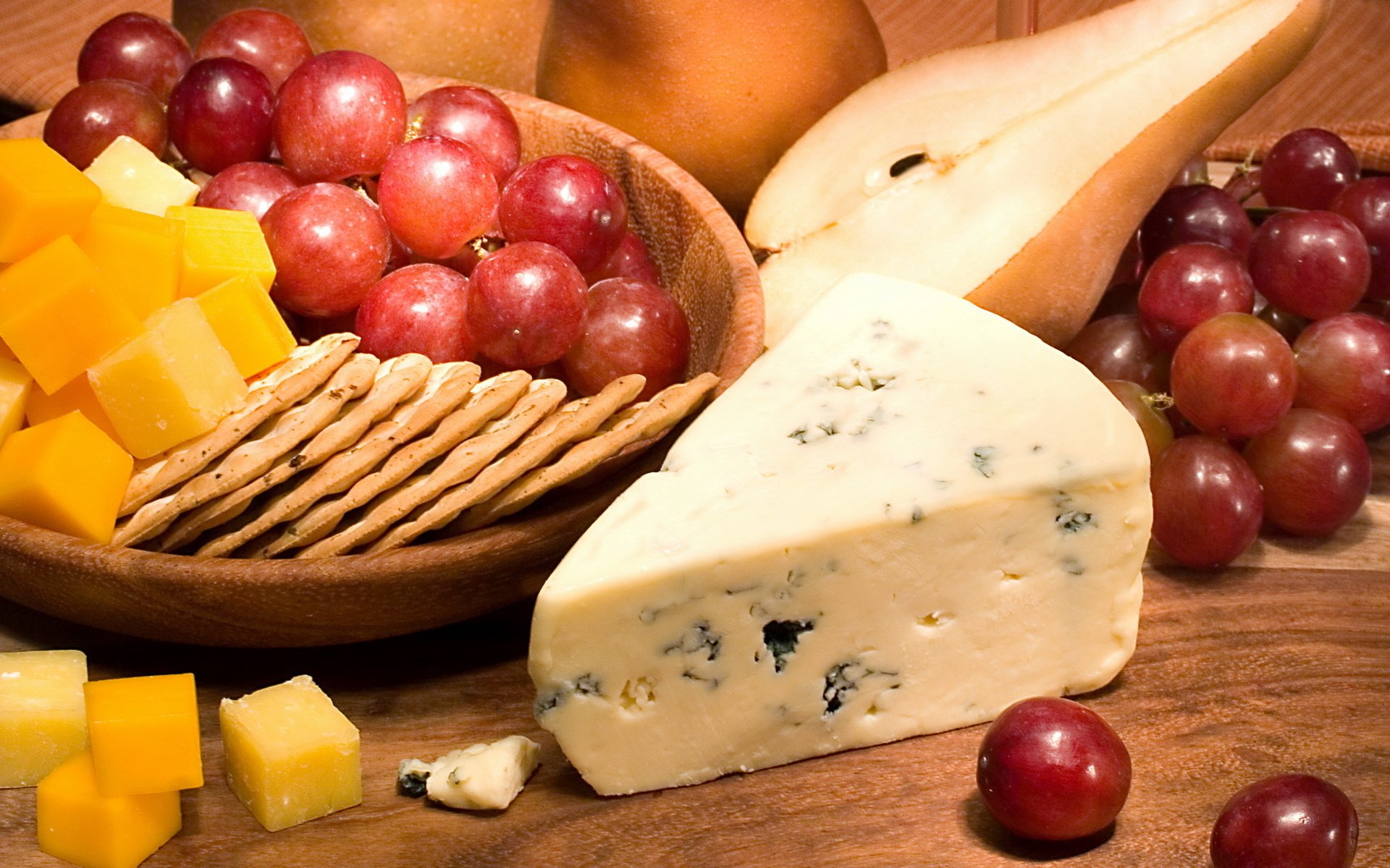 HD desktop wallpaper featuring a still life of cheese cubes, blue cheese, red grapes, and crackers arranged on a wooden surface.