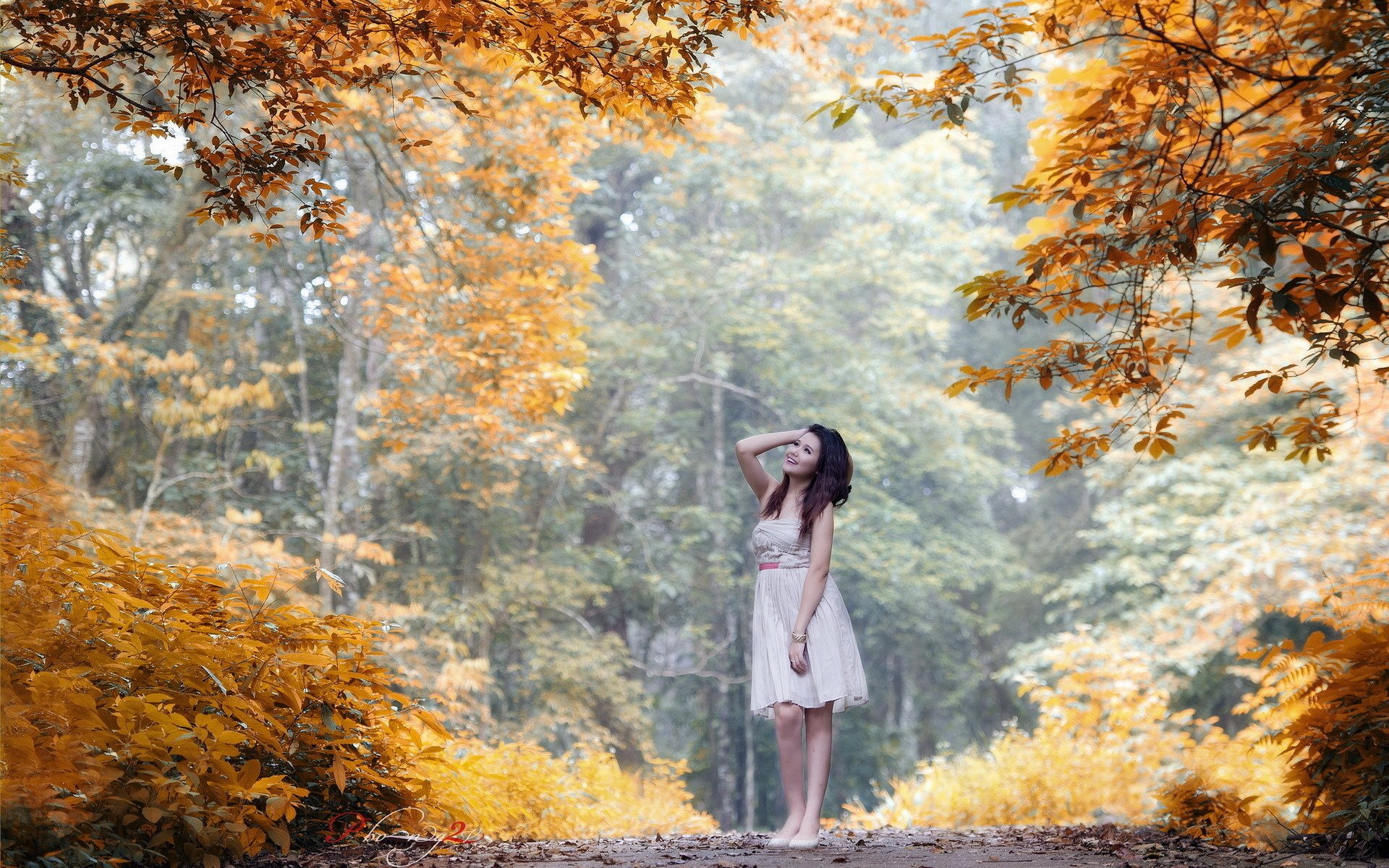 A woman in a white dress stands among vibrant autumn foliage, creating a serene and reflective mood. This HD desktop wallpaper showcases the tranquility of nature's fall colors.