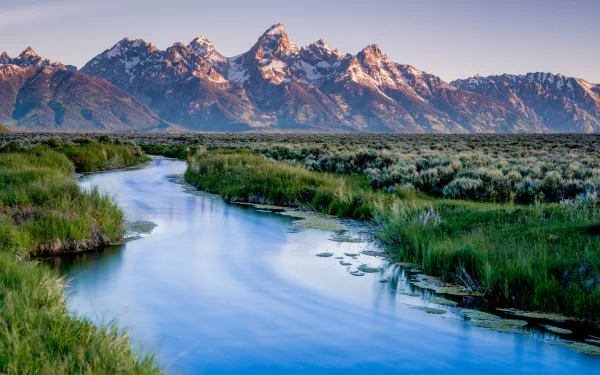 HD desktop wallpaper showcasing a serene river winding through lush greenery with the majestic peaks of Grand Teton National Park in the background.